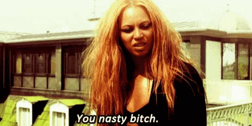 a woman with long red hair is standing in front of a building and saying you nasty bitch .