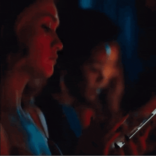 two women are looking at their cell phones in the dark