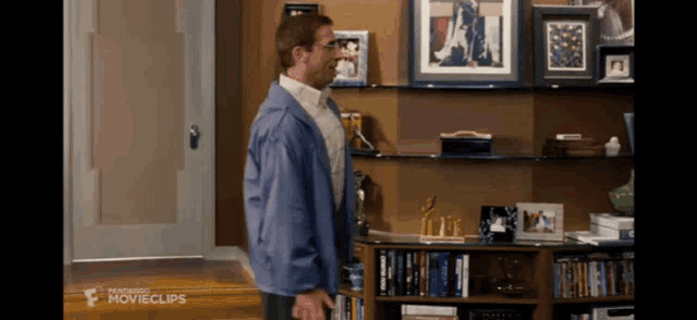 a man in a blue jacket stands in front of a bookshelf that says movieclips on the bottom