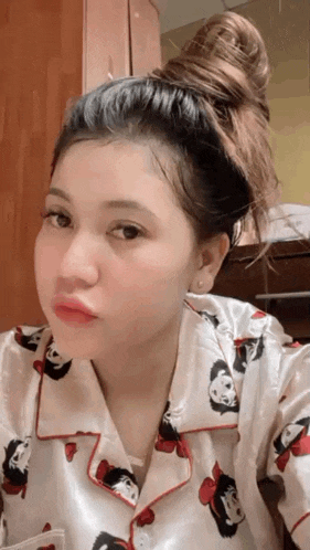a woman wearing a pajama top with a bun in her hair is taking a selfie .