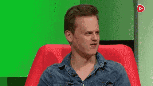 a man in a denim shirt is sitting in a red chair with a green background .