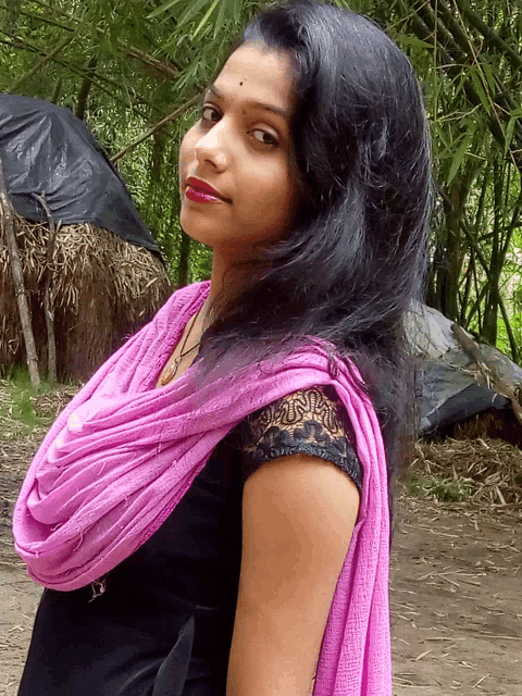 a woman wearing a black top and a pink scarf stands in a forest