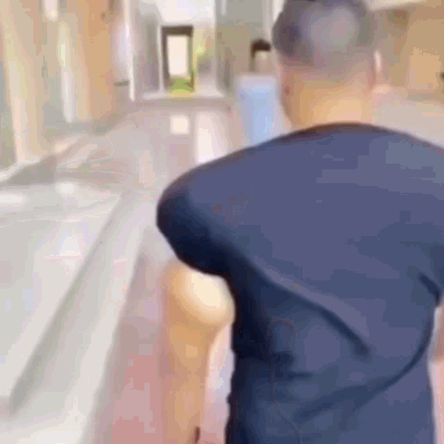 a man in a blue shirt is walking down a hallway with a blurred background .