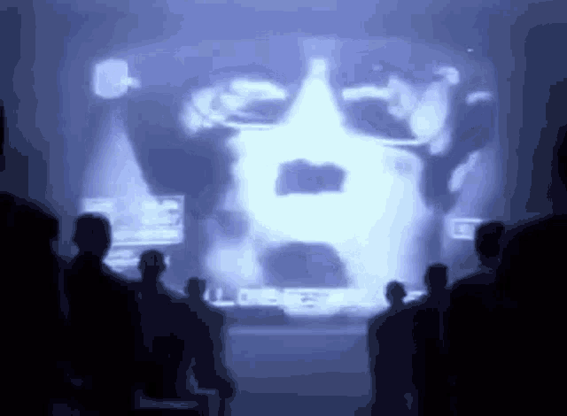a group of people are standing in front of a large screen with a picture of a man on it .