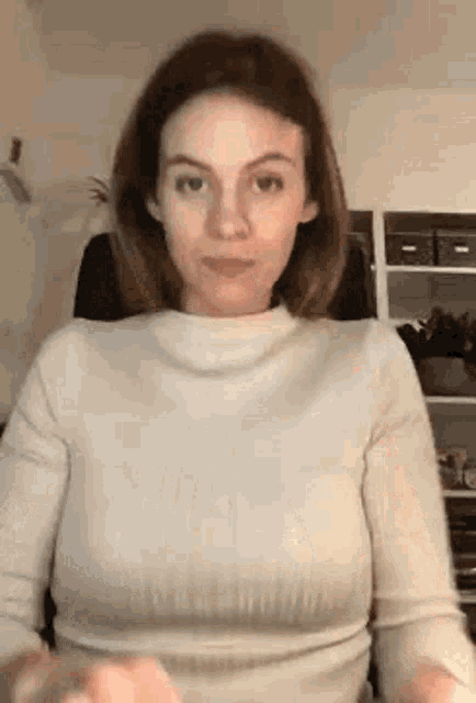 a woman in a white sweater is sitting in a chair and making a face .