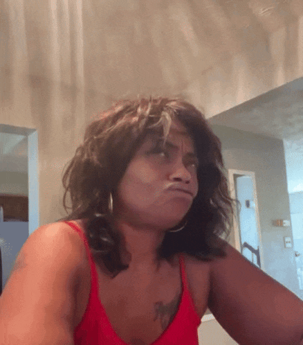 a woman in a red tank top is making a funny face .