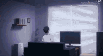 a man is sitting on a couch in a living room with a computer and a television .