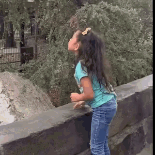 a little girl is standing on a ledge looking up at a tree