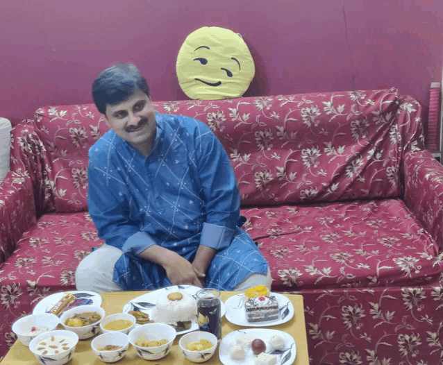 a man in a blue shirt sits on a couch with plates of food