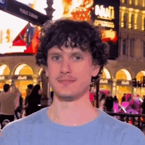 a man with curly hair and a mustache is standing in front of a crowd of people on a city street .