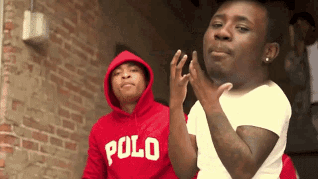 a man wearing a red polo hoodie stands next to another man in a white shirt