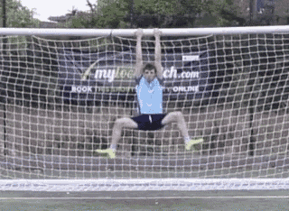 a man is hanging from a soccer goal with a sign behind him that says mycoach.com
