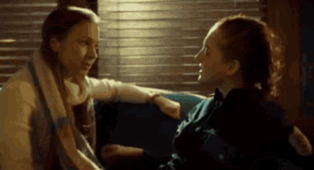 two women are sitting next to each other on a couch and talking .