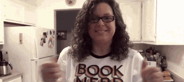 a woman wearing glasses and a book nerd shirt is smiling