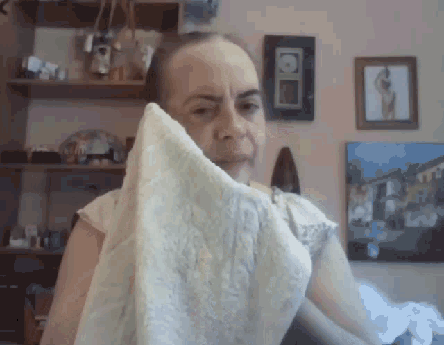 a woman wipes her face with a towel in front of a wall with pictures on it