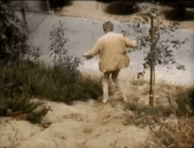 a man in a yellow coat is running down a dirt path .
