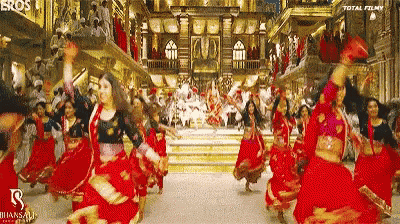 a group of women in red dresses are dancing in front of a crowd .