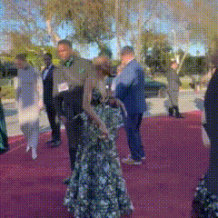 a woman in a floral dress is standing on a red carpet with other people