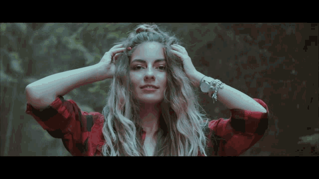 a woman wearing a plaid shirt and bracelets adjusts her hair