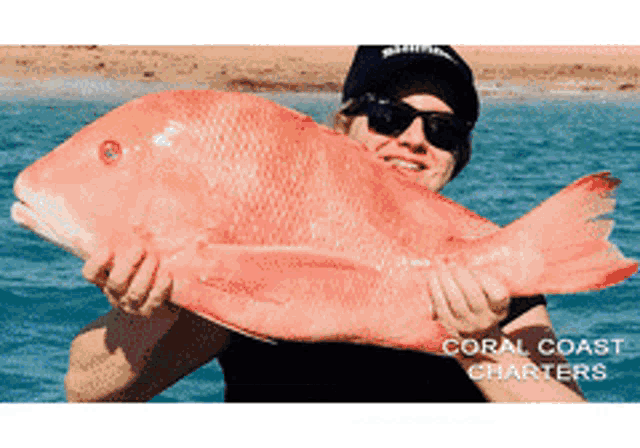 a man is holding a large red fish with the words coral coast charters below him