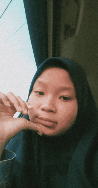 a girl wearing a blue hijab looks at the camera with her hand on her chin