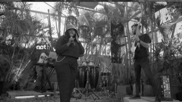 a black and white photo of a woman singing into a microphone while a man plays a guitar .