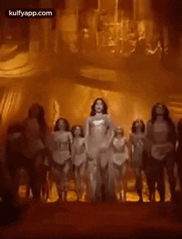a woman in a white dress is dancing on a stage with a group of dancers .