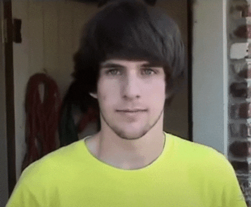 a young man wearing a yellow shirt with a beard looks at the camera