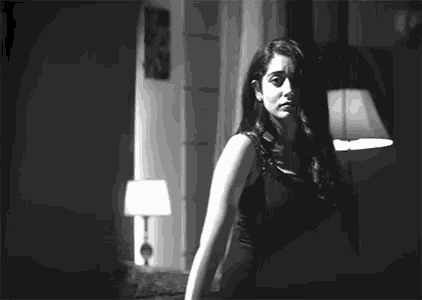 a black and white photo of a woman standing in a dark room with a lamp .