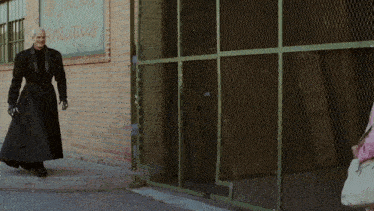 a woman in a long black coat stands in front of a building with a sign that says antiques