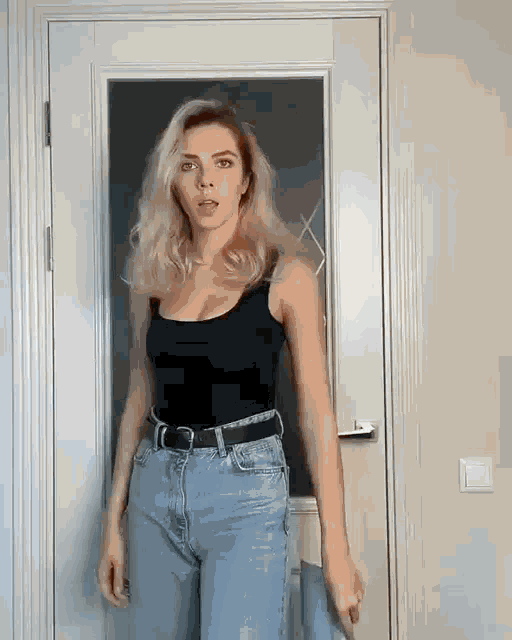 a woman is standing in front of a door wearing jeans and a black tank top .