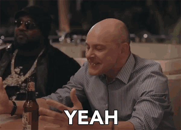 a bald man is sitting at a table with a bottle of beer and saying yeah