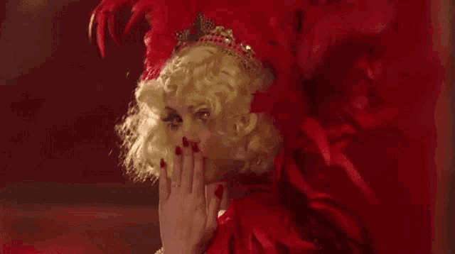 a woman in a red feathered costume with a crown on her head is blowing a kiss .