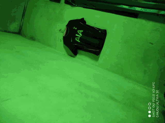 a black shirt with aia written on it hangs on a green wall