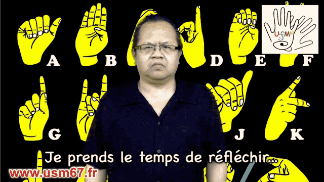 a man with glasses stands in front of a sign language alphabet