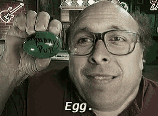 a man wearing glasses is holding a green egg that says `` egg '' .