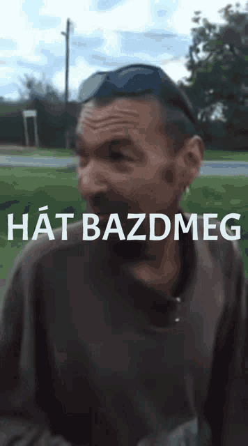 a man wearing sunglasses stands in front of a sign that says hat bazdmeg on it