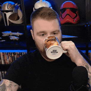 a man drinking from a star wars mug in front of a storm trooper helmet