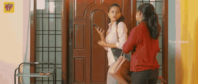 two women are standing in front of a door and one is holding a cell phone