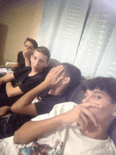 a group of young men are sitting on a couch and one of them is wearing a white shirt with a picture of a bear