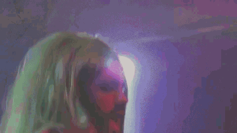 a man with long green hair and a beard is singing into a microphone in a dark room .