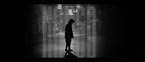 a black and white photo of a person in a hooded jacket standing in a dark street