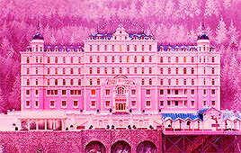 a large pink building with trees in the background and a bridge in front of it