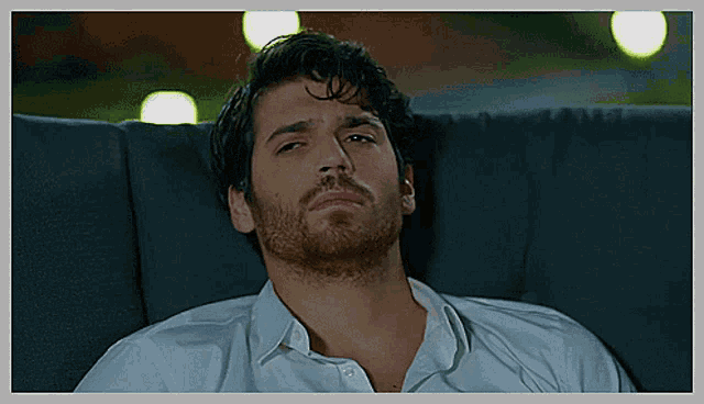 a man with a beard and a white shirt is laying on a couch