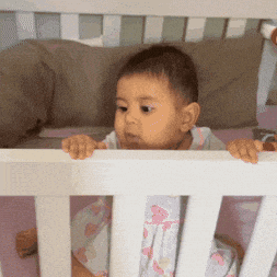 a baby is sitting in a crib looking over the railing
