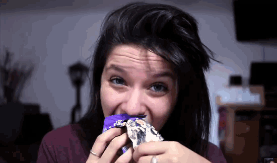 a woman with a ring on her finger is eating a candy bar with a purple label