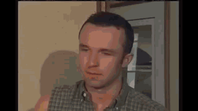 a man in a plaid shirt is making a funny face while standing in front of a window .