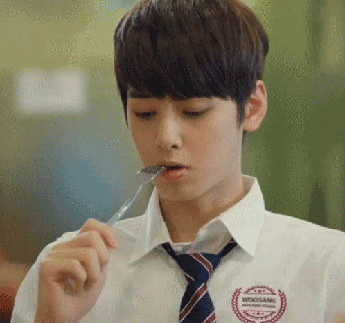 a young man wearing a woosang shirt and tie is eating something with a spoon in his mouth