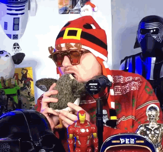 a man wearing a santa hat and sunglasses is holding a squirrel in his mouth