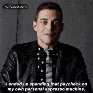 a man in a leather jacket and tie is smiling and talking about spending that paycheck on his own personal espresso machine .